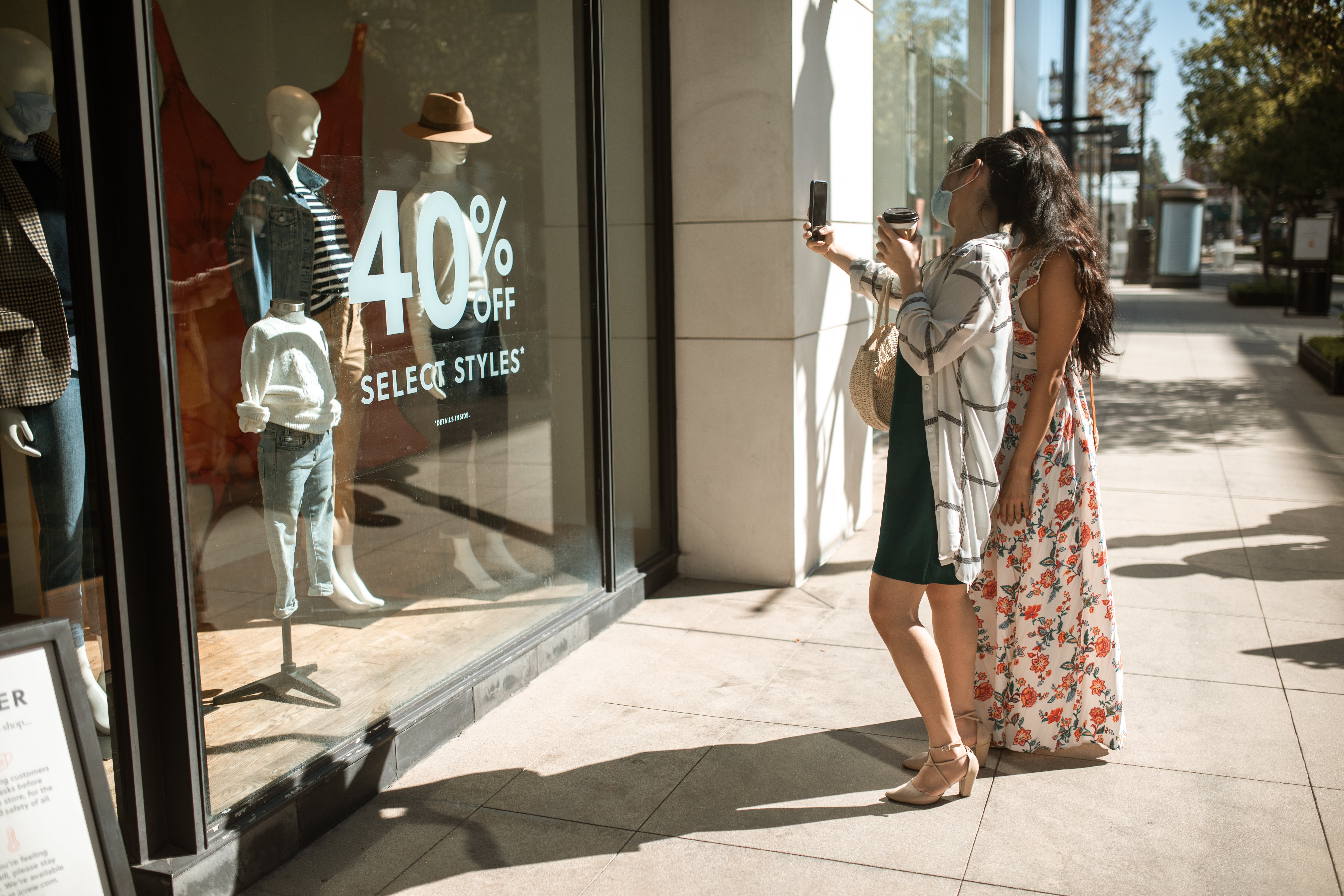 two shoppers in sundresses admire clothing in a window display